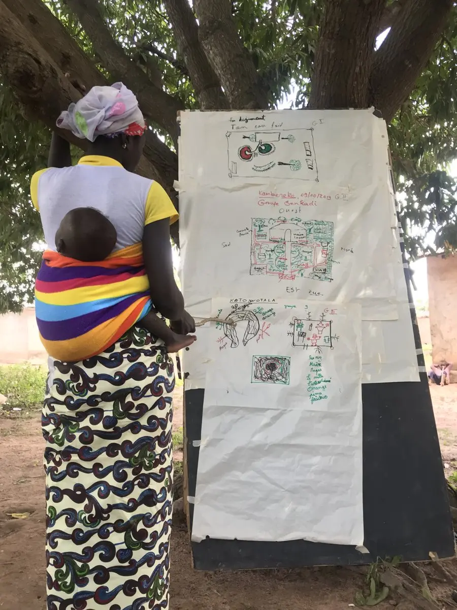 Community member reviewing a hand-drawn site plan during a mapping session in Kambereke